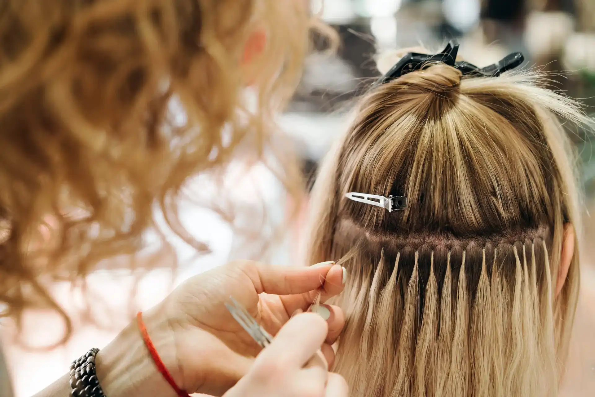 Hair extensions being applied to a woman's blonde hair in a salon.