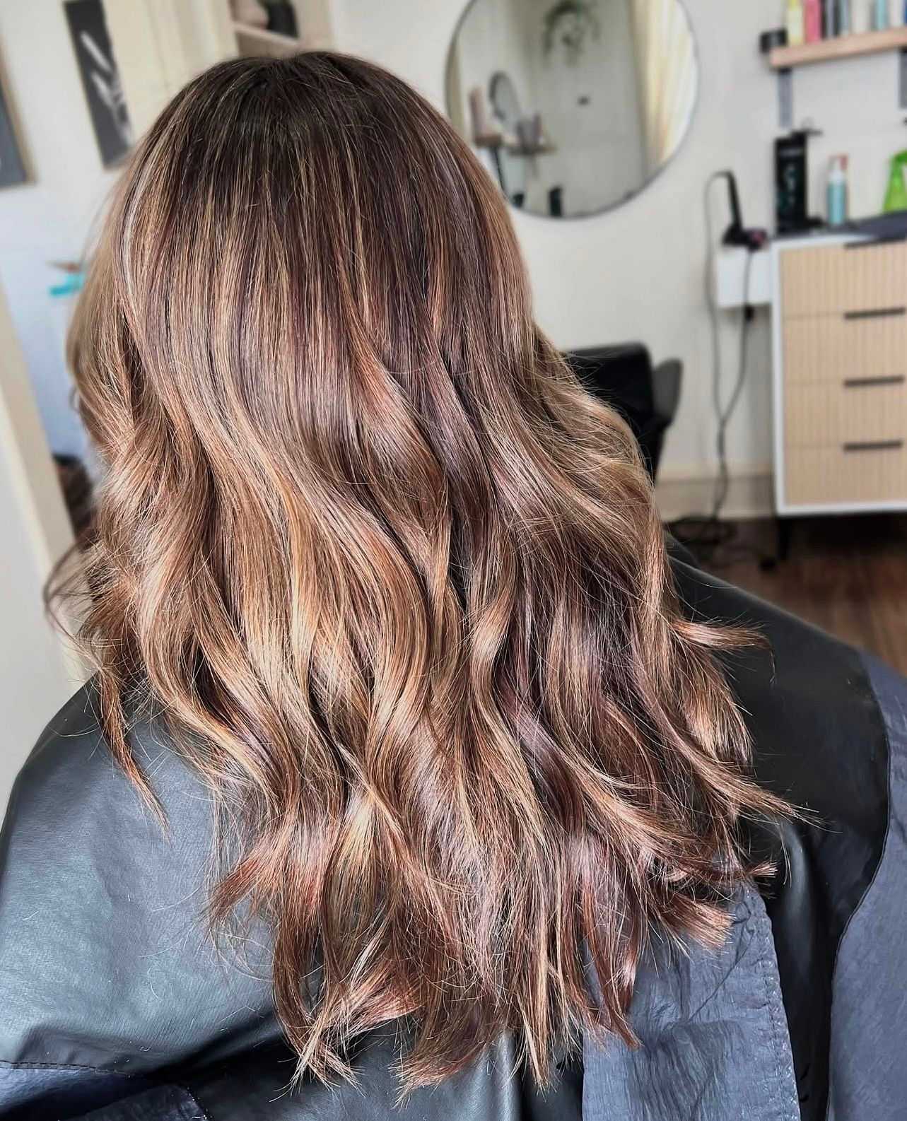 Wavy brown hair with blonde highlights styled in a salon.