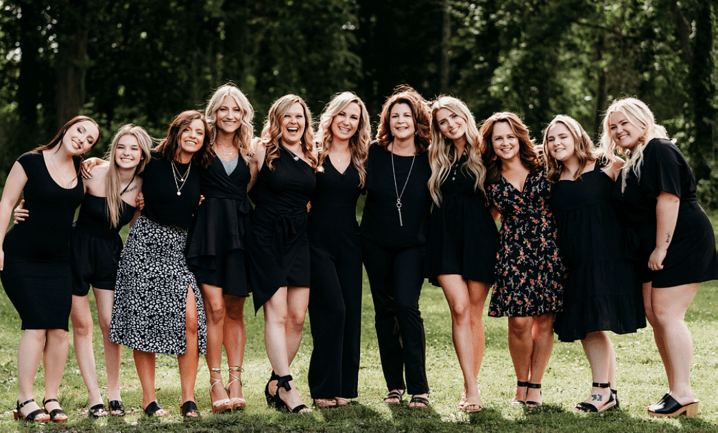 A group of smiling women standing together outdoors, all dressed in black outfits.